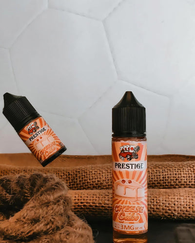Two bottles of Prestige Cheese Cakes vape juice on a textured surface with a white geometric patterned wall in the background.